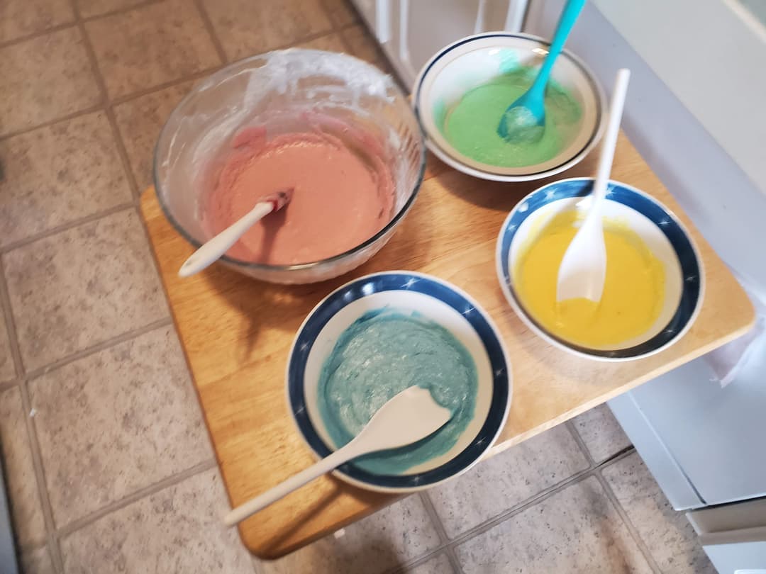 Four different size bowls full of icing colored green, pink, yellow, blue
